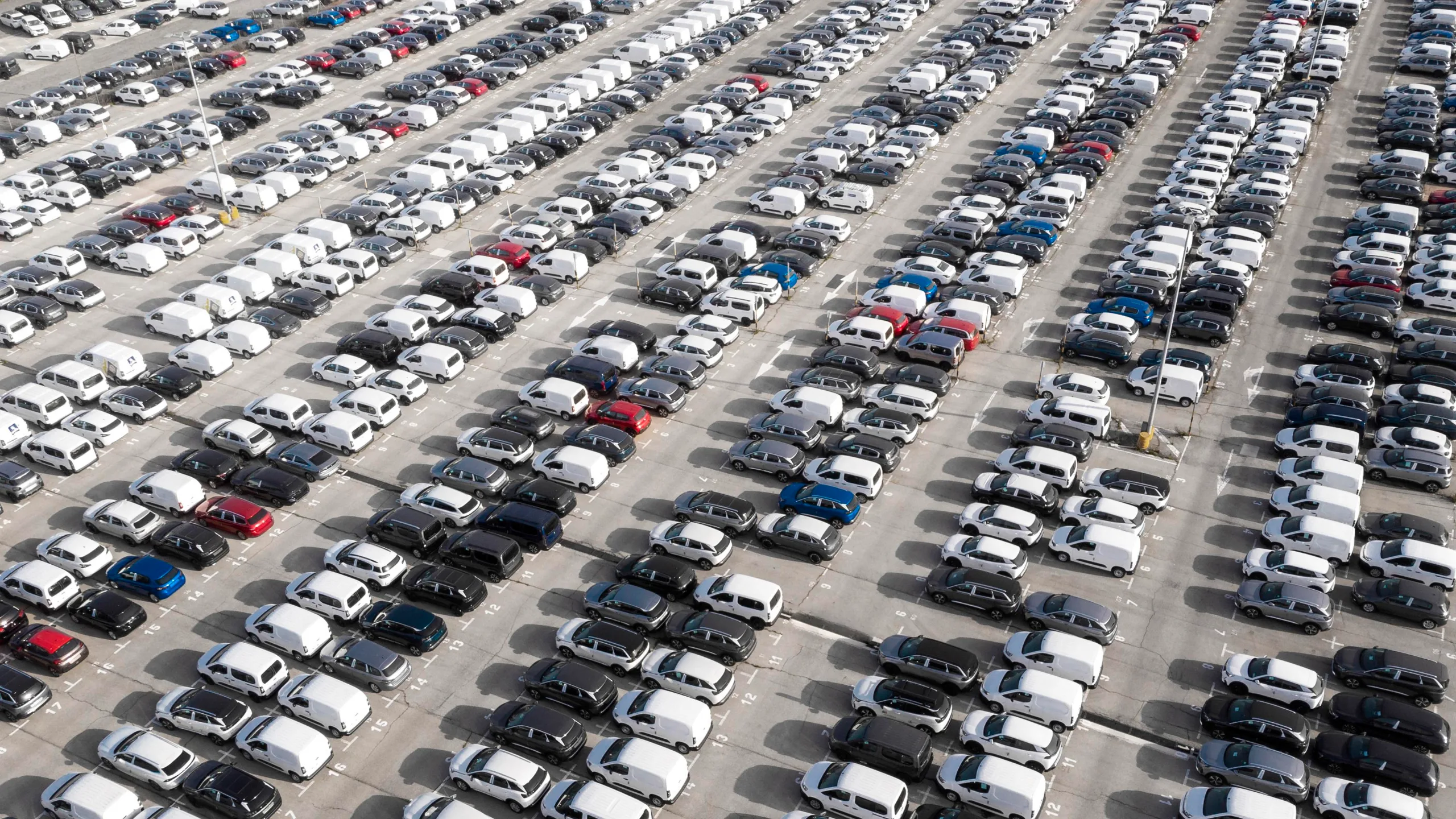 Vue aérienne d’un parc de véhicules d’entreprise, voitures particulières et utilitaires légers alignés en rangées, illustrant la gestion de flotte en location longue durée